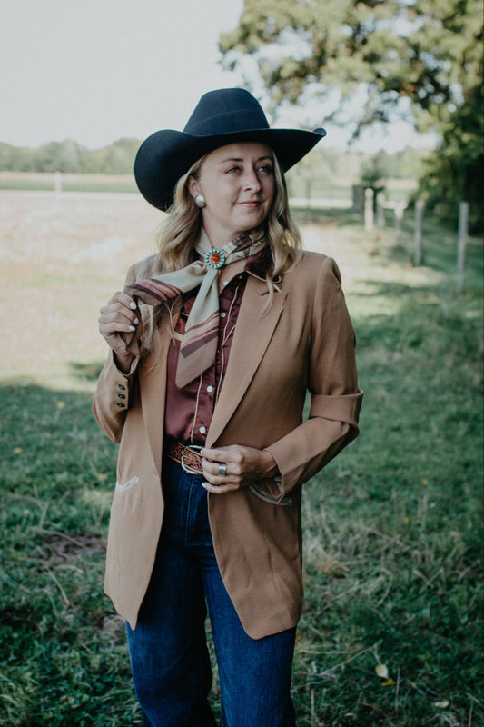 Woman in a brown coat and black hat standing in a grassy field.